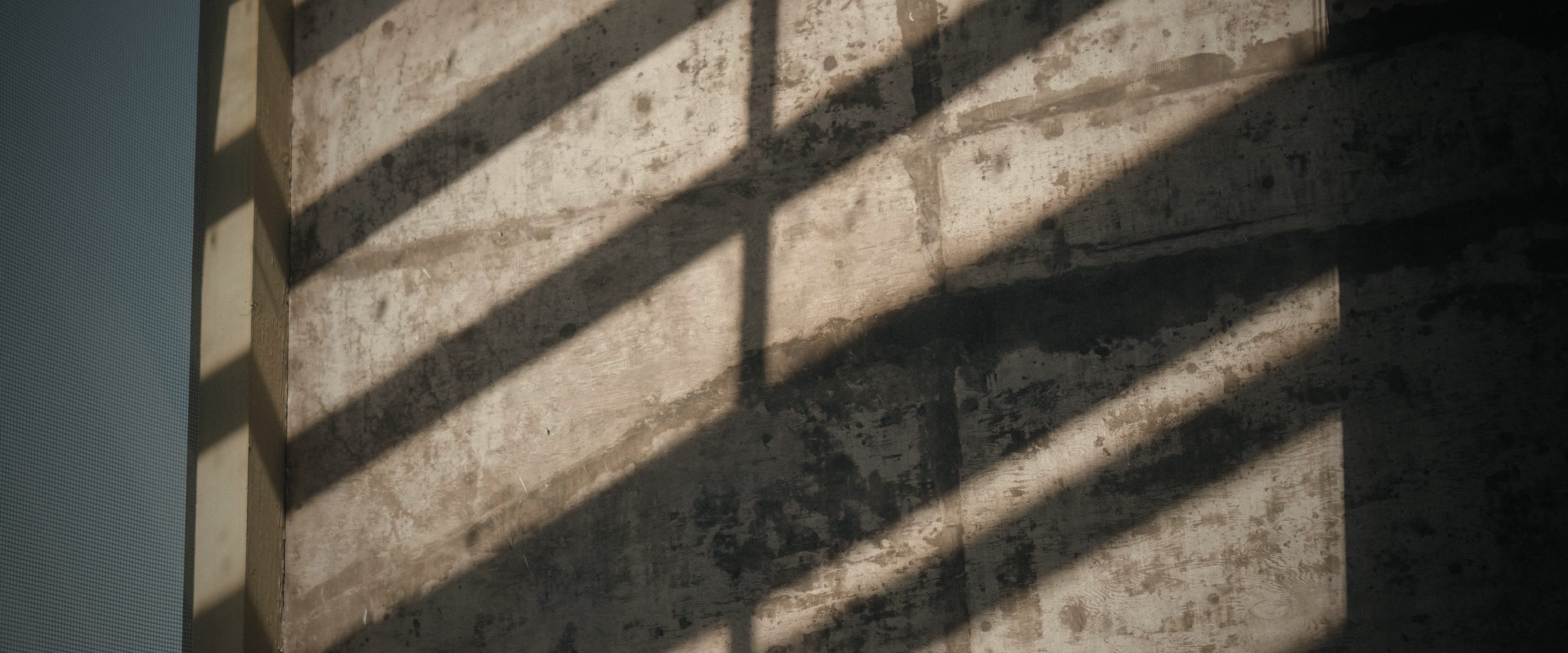 Diagonal shafts of sunlight and shadow crossing a textured concrete wall